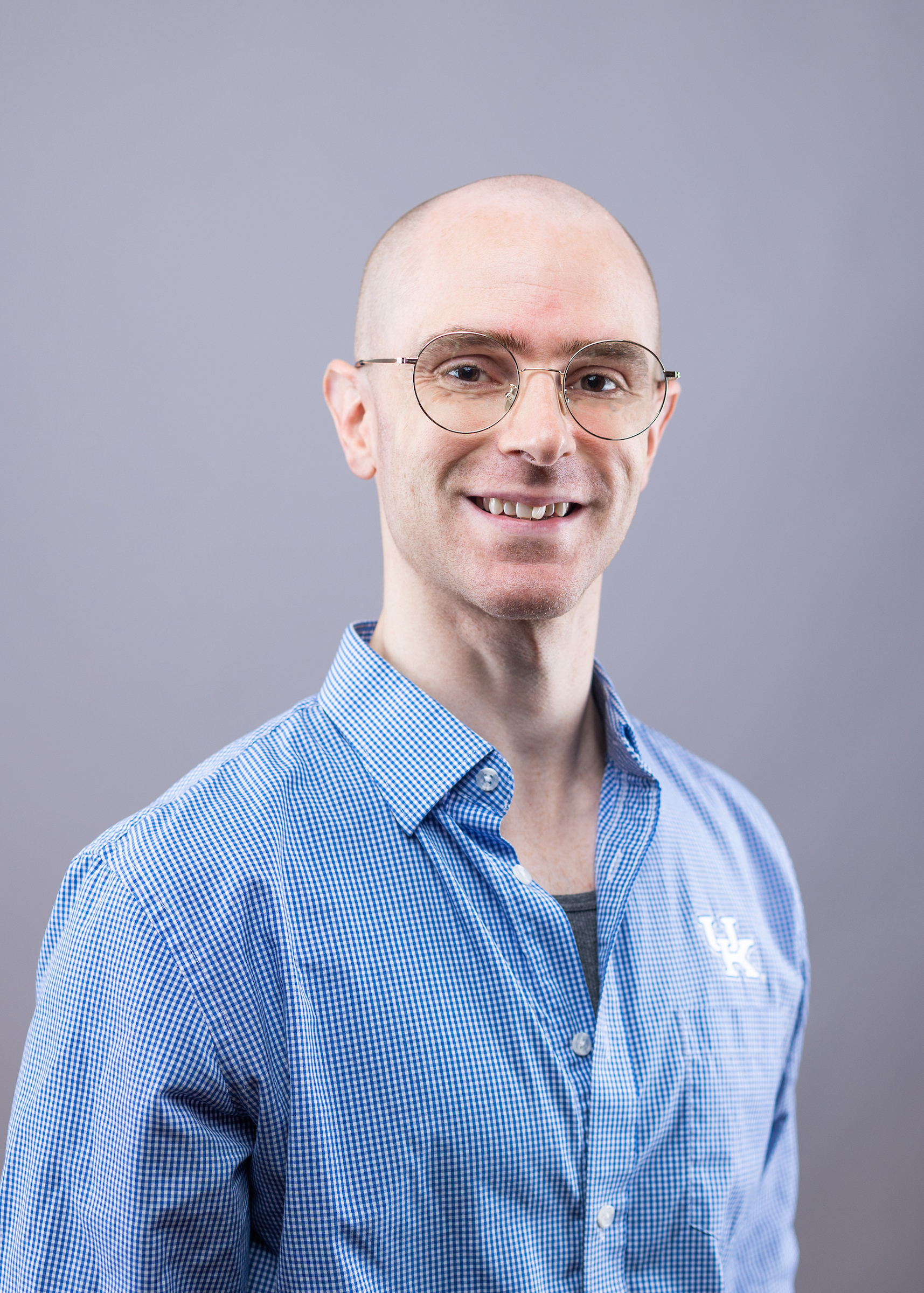 Recruiter Addison Mills smiling wearing a blue checkered button up shirt and gold-rimmed glasses